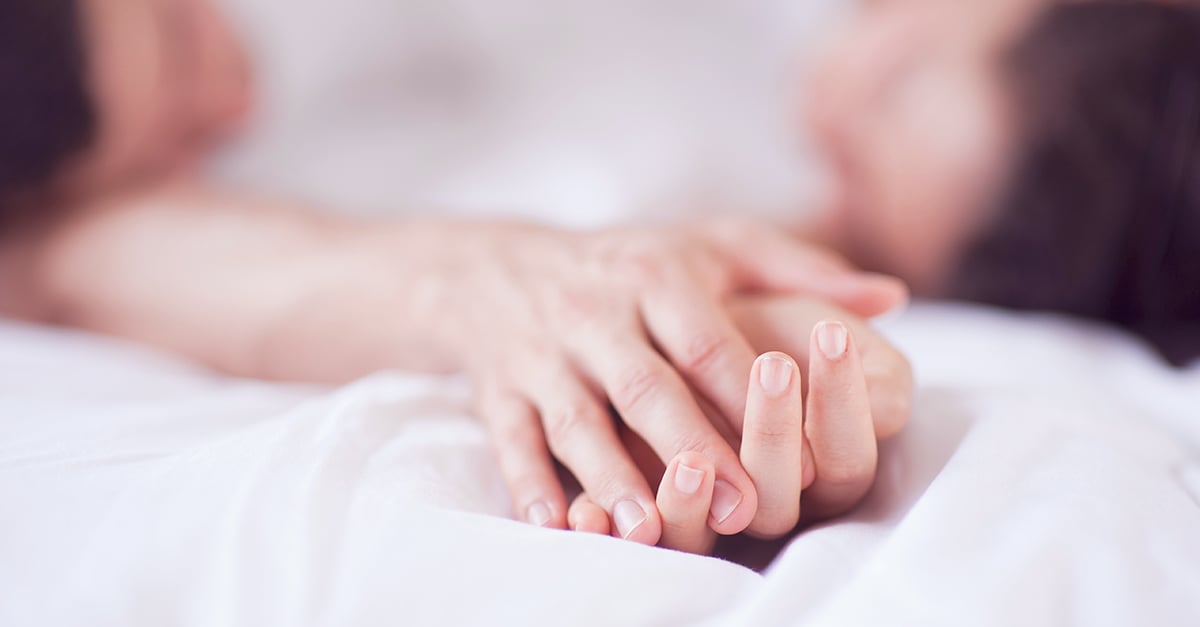 Hände ineinandergeschlungen auf weißen Bettlaken