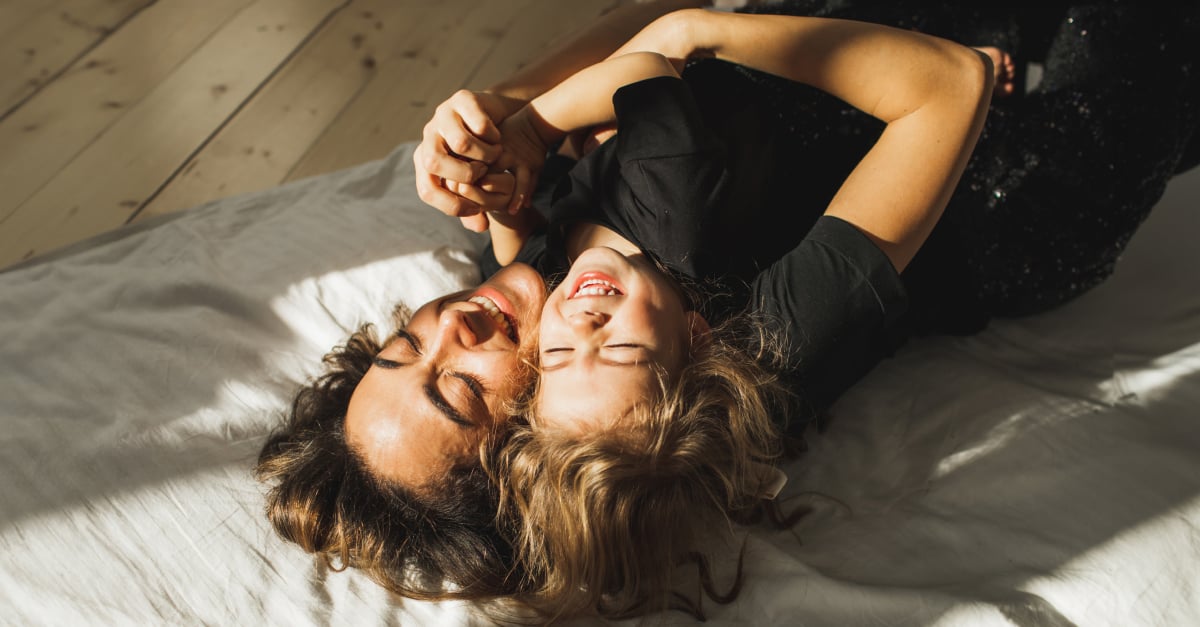 Eine Frau und ein Kind mit braunen Locken liegen auf dem Rücken und umarmen sich.