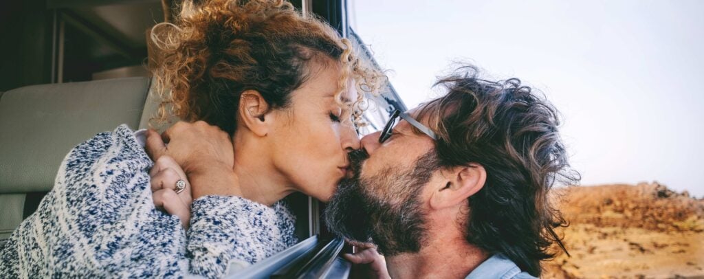 Frau und Mann küssen sich durch ein geöffnetes Autofenster.