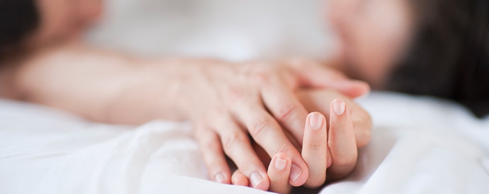 zwei Hände berühren sich sinnlich auf einem weißen Bettlaken