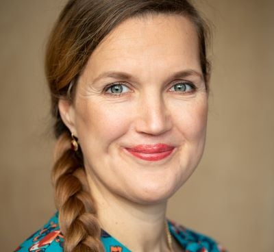 Portraitfoto von Dania Schiftan. Sie trägt einen langen, geflochtenen Zopf und auffälligen, roten Lippenstift.
