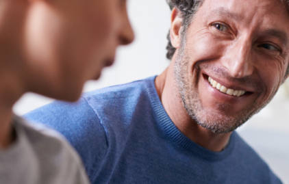 Ein etwa Mitte Vierzig jähriger Mann mit einem angegrauten Dreitagebart lächelt seinen Sohn an.