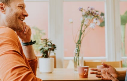 Ein Mann und eine Frau lachen gemeinsam beim Kaffeetrinken.
