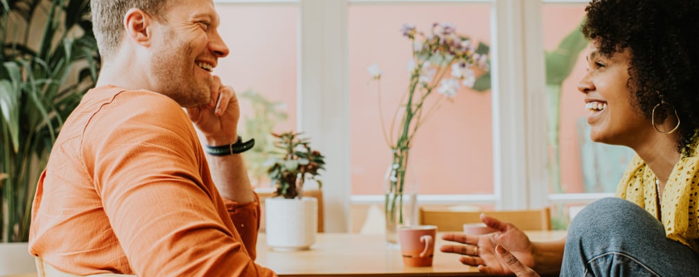 Ein Mann und eine Frau lachen gemeinsam beim Kaffeetrinken.