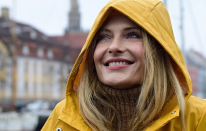 Eine Frau in einem gelben Mantel lächelt glücklich.